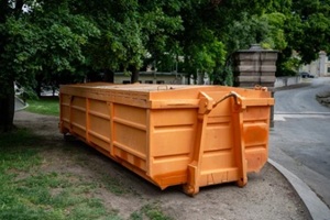 large orange industrial construction dumpster placed under trees in Hampton Roads, VA 
