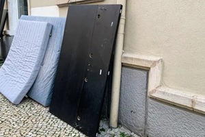mattress and black panel leaning against building, urban waste management
