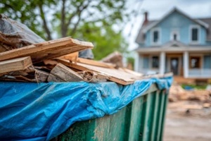 construction dumpster filled with wooden debris and covered with blue tarp in front of a house undergoing renovation on a cloudy day