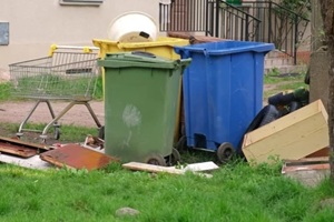old discarded household furniture dumped by colorful plastic dumpsters for bulk item pickup by city cleaning services