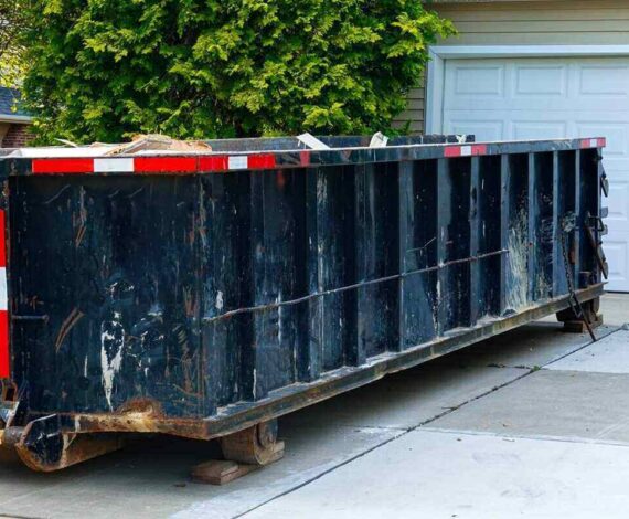 blue dumpster full of wood and other debris in the driveway in front of a house in the suburbs that is being renovated