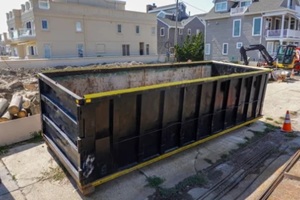  empty black dumpster is seen at a construction site near a backhoe