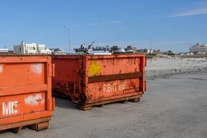 two orange dumpsters at construction site on a wet sandy beach that say rent me on them