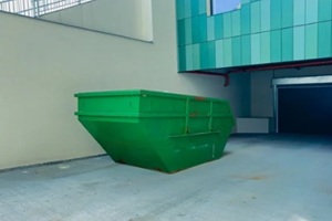 large green dumpster sits on concrete floor in an outdoor area of a building during daytime