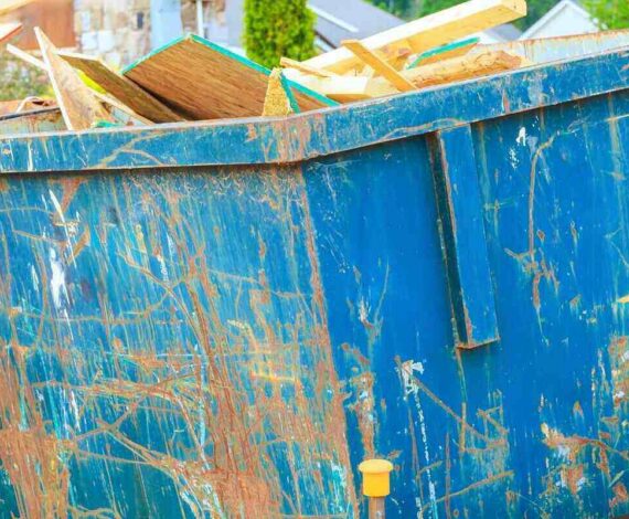 workers place wood debris into large blue dumpster near construction site in residential neighborhood