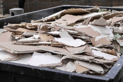 an overloaded dumpster waste container, with construction waste and drywall plasterboard, debris generated during the reconstruction process