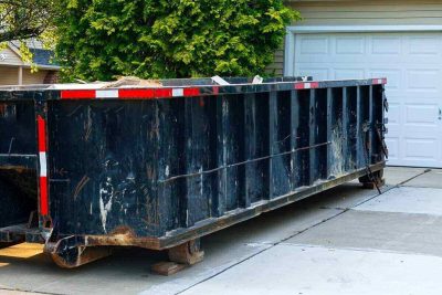blue dumpster full of wood and other debris in the driveway in front of a house in the suburbs that is being renovated