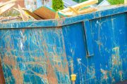 workers place wood debris into large blue dumpster near construction site in residential neighborhood
