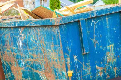 workers place wood debris into large blue dumpster near construction site in residential neighborhood